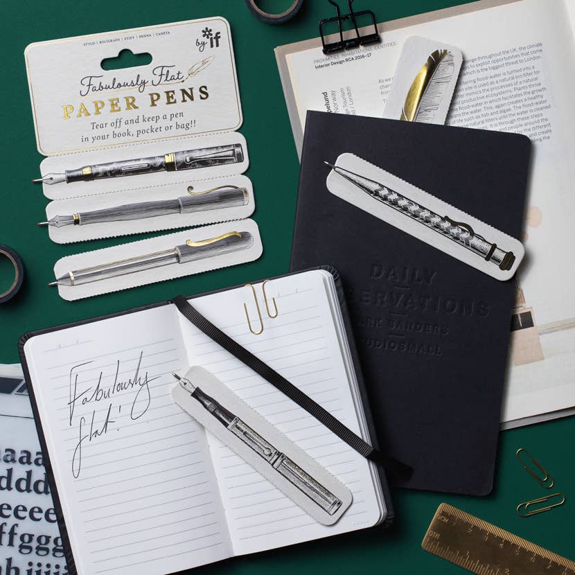 Three paper pens torn from the card beside a notebook, one keeping the page as a bookmark
